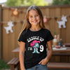 Young girl wearing a black t-shirt with a cowboy design and text, standing outdoors.
