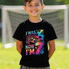 Child wearing a black t-shirt with colorful text 6 7 and numbers, standing in front of a soccer goal.