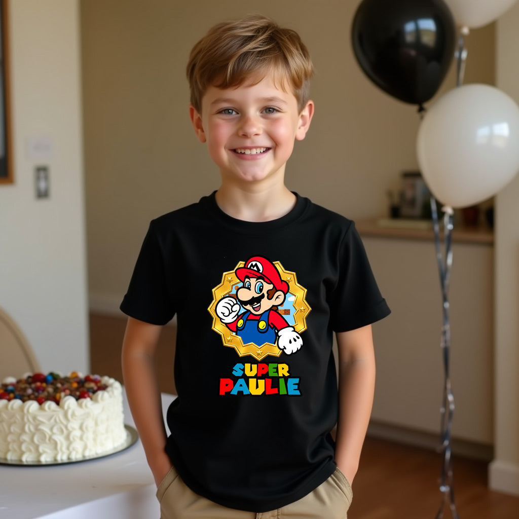 Child wearing a black t-shirt with a colorful graphic and text, standing in a room with balloons and a cake.