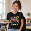 Person wearing a black t-shirt with colorful 'Book Week Energy' design in a classroom setting.