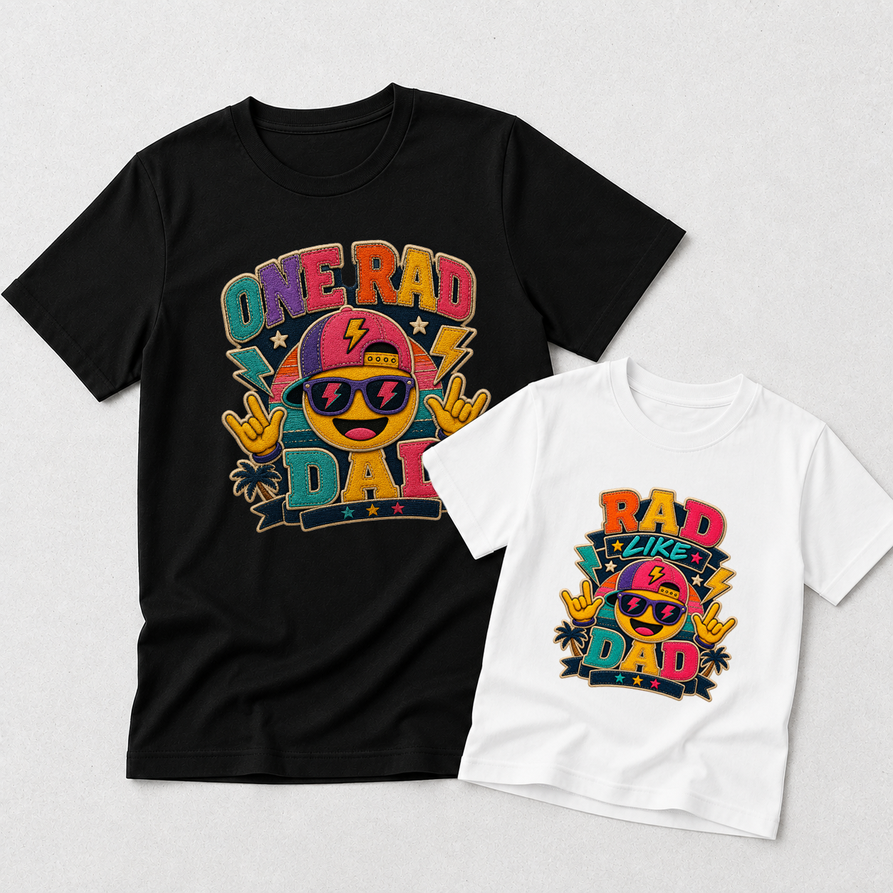 A black adult T-shirt and a white child T-shirt, both laid flat on a light gray background. Each shirt features a colorful retro-style graphic with the text 'ONE RAD DAD' on the larger shirt and 'RAD TAKES DAD' on the smaller shirt, plus a smiling face wearing sunglasses and palm trees.