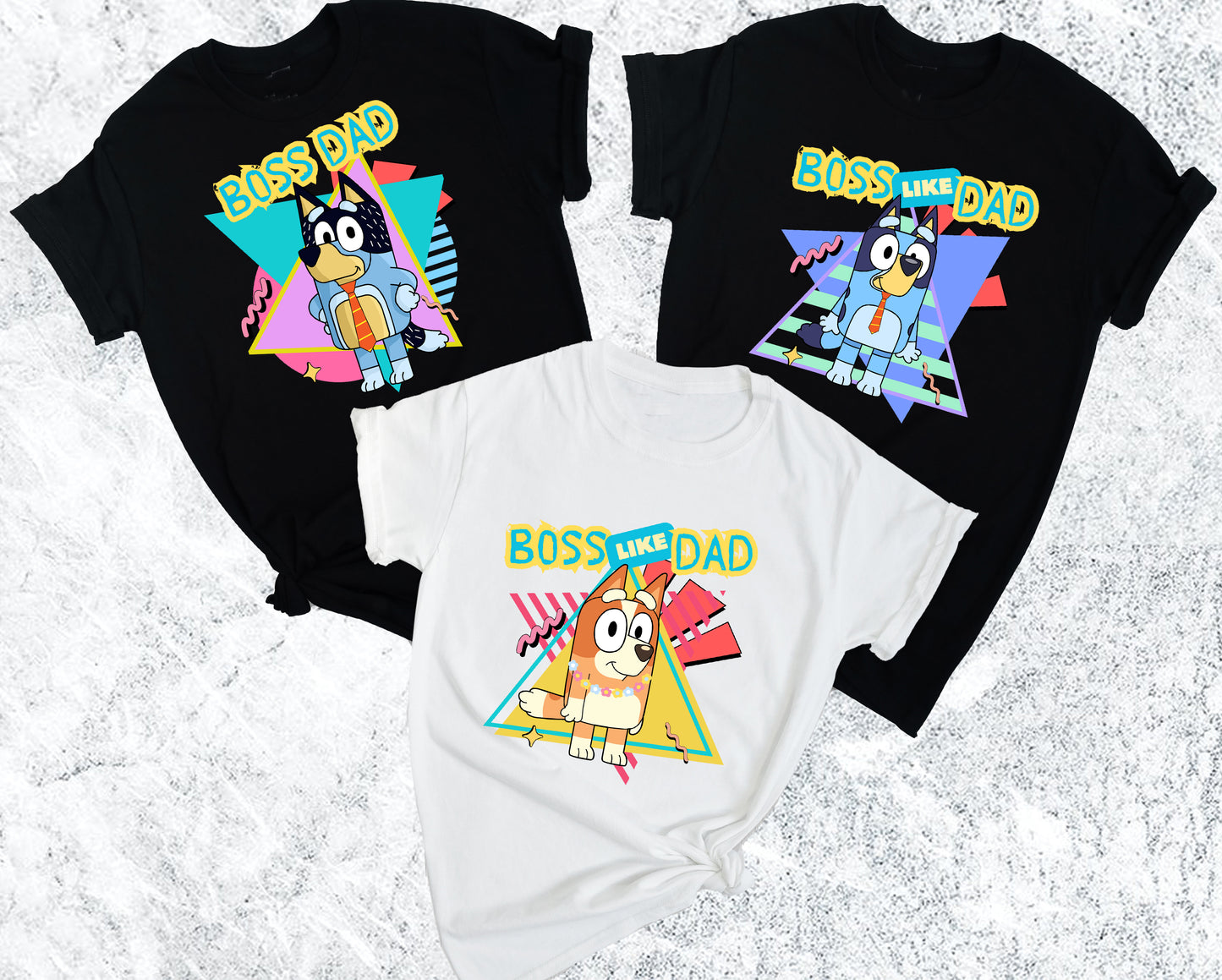 Two black t-shirts and a white onesie with 'Boss Like Dad' graphic design on a textured surface.