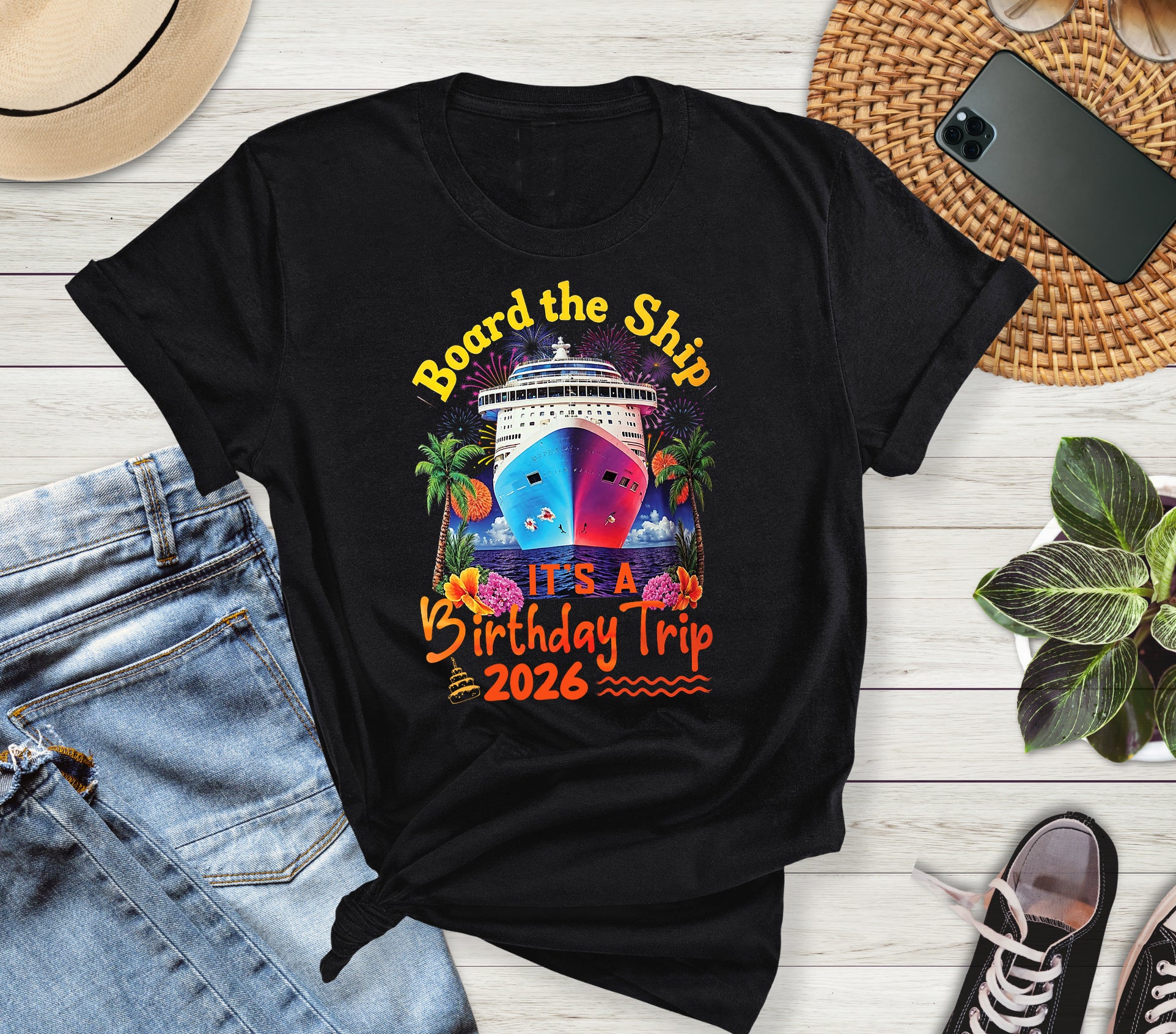 Black t-shirt with colorful ship graphic and text 'Board the Ship It's a Birthday Trip 2026' on a wooden surface with jeans and shoes.