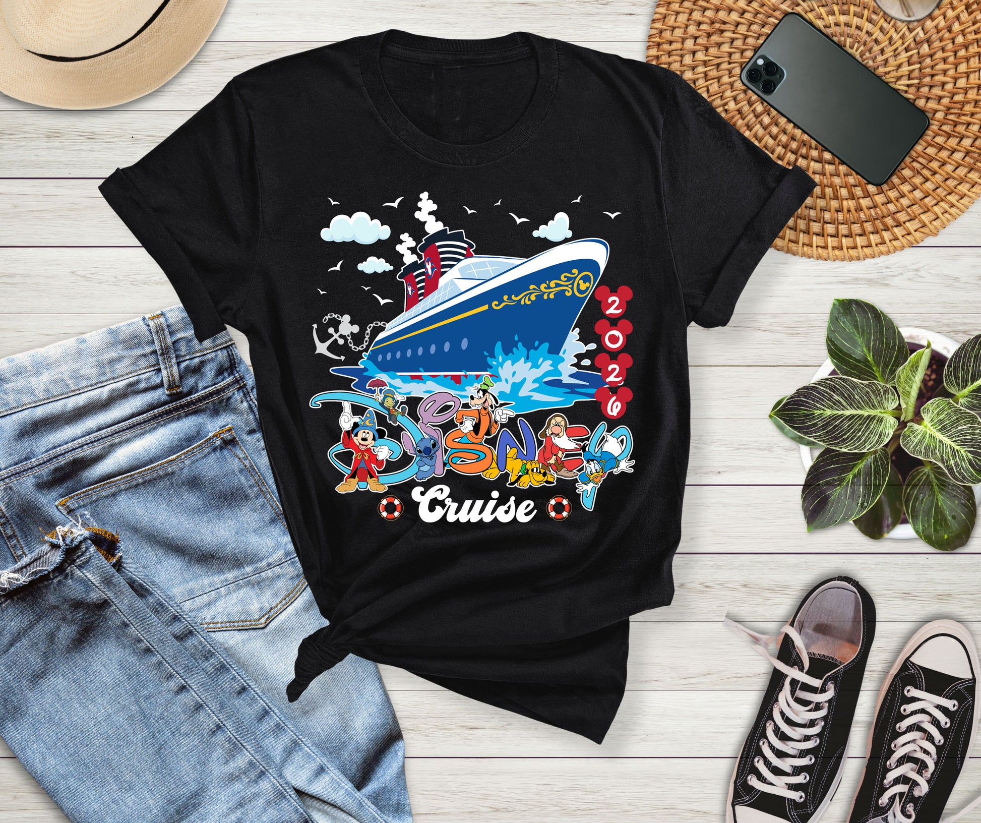 Black t-shirt with cruise ship graphic on a wooden surface with jeans, sneakers, and a phone.