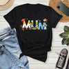 Black t-shirt with colorful 'MUM' design on a wooden surface with jeans, sneakers, and a phone.