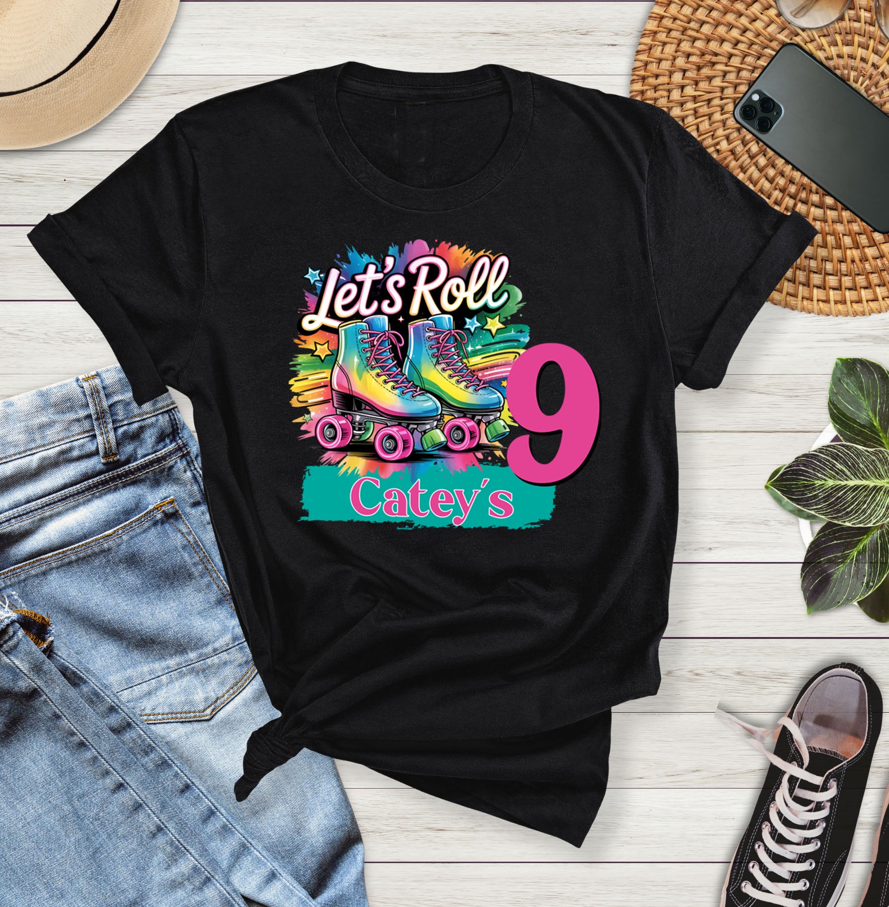 Black t-shirt with colorful graphic and text on a wooden surface with jeans and sneakers.