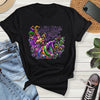 Black t-shirt with colorful Mardi Gras design on a wooden surface with jeans and sneakers.