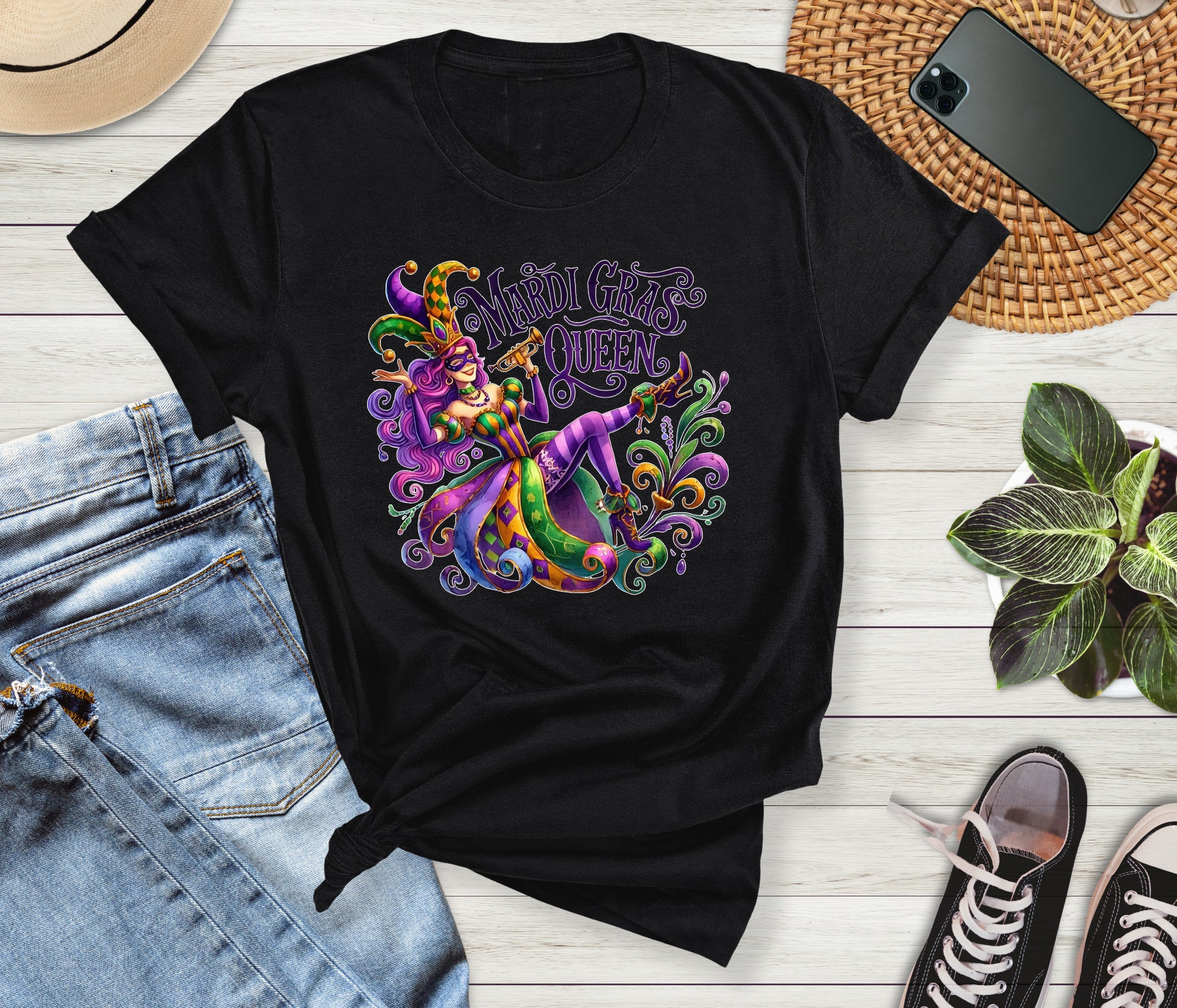 Black t-shirt with colorful Mardi Gras design on a wooden surface with jeans and sneakers.
