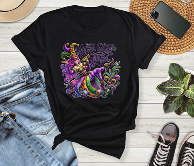 Black t-shirt with colorful Mardi Gras design on a wooden surface with jeans and sneakers.