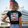 Person wearing a black t-shirt with a colorful graphic design in front of a cruise ship.