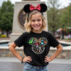 Young girl wearing a black t-shirt with colorful graphics and text, standing outdoors.