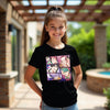 Young girl wearing a black t-shirt with colorful graphic design outdoors.