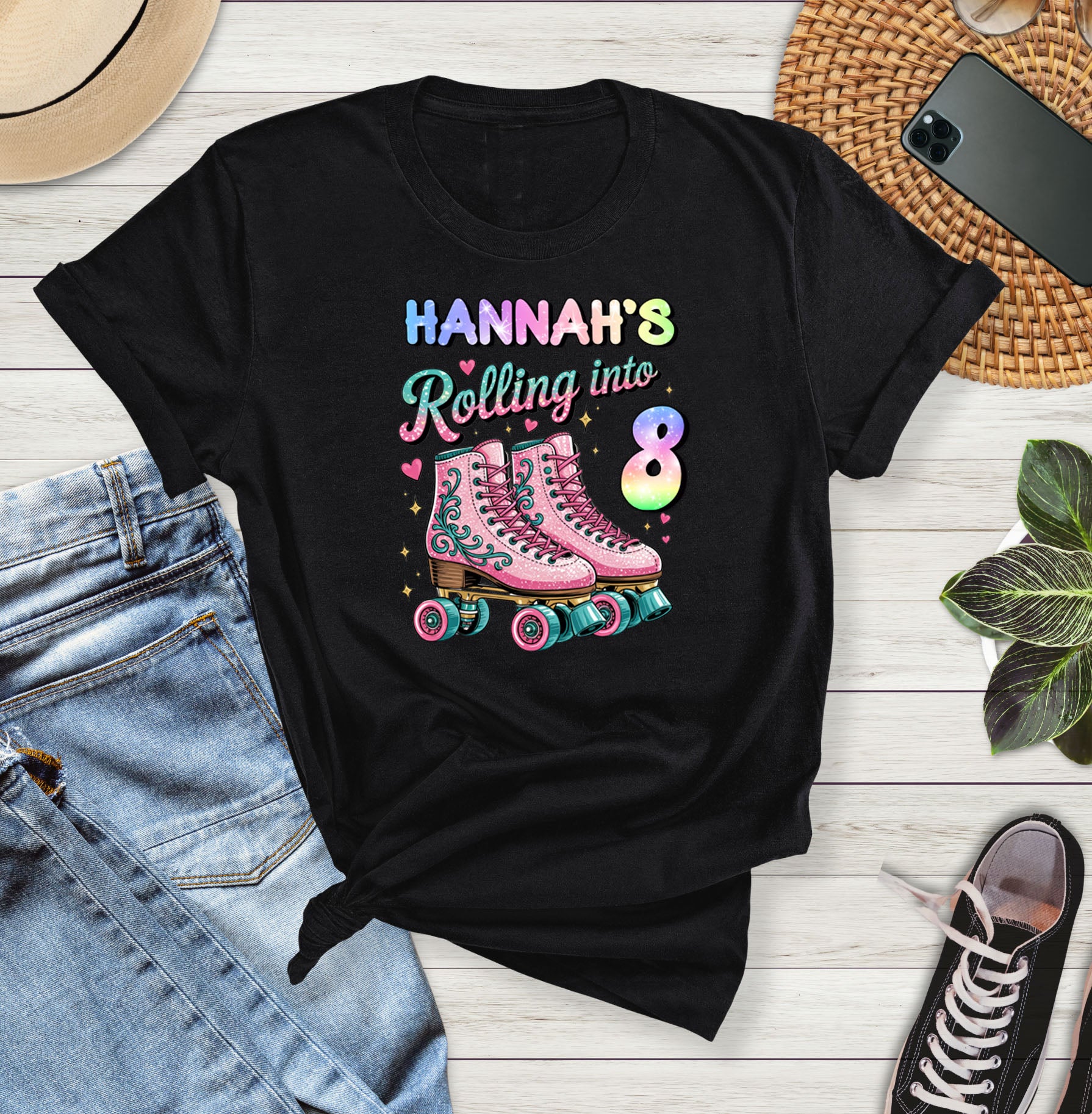 Black t-shirt with 'Hannah's Rolling into 8' design on a wooden surface with jeans and sneakers.