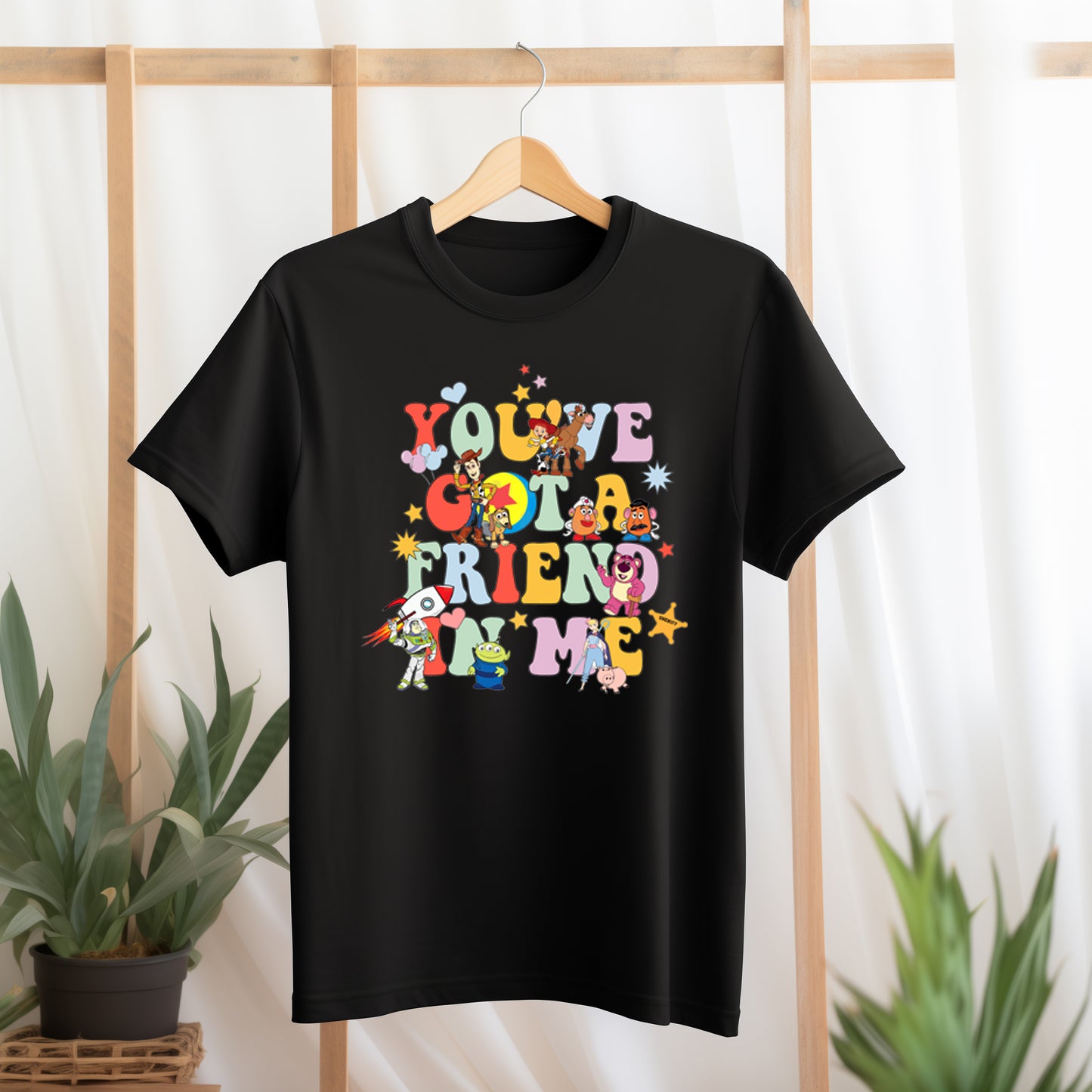 Black t-shirt with colorful text and character graphics on a hanger against a light background.