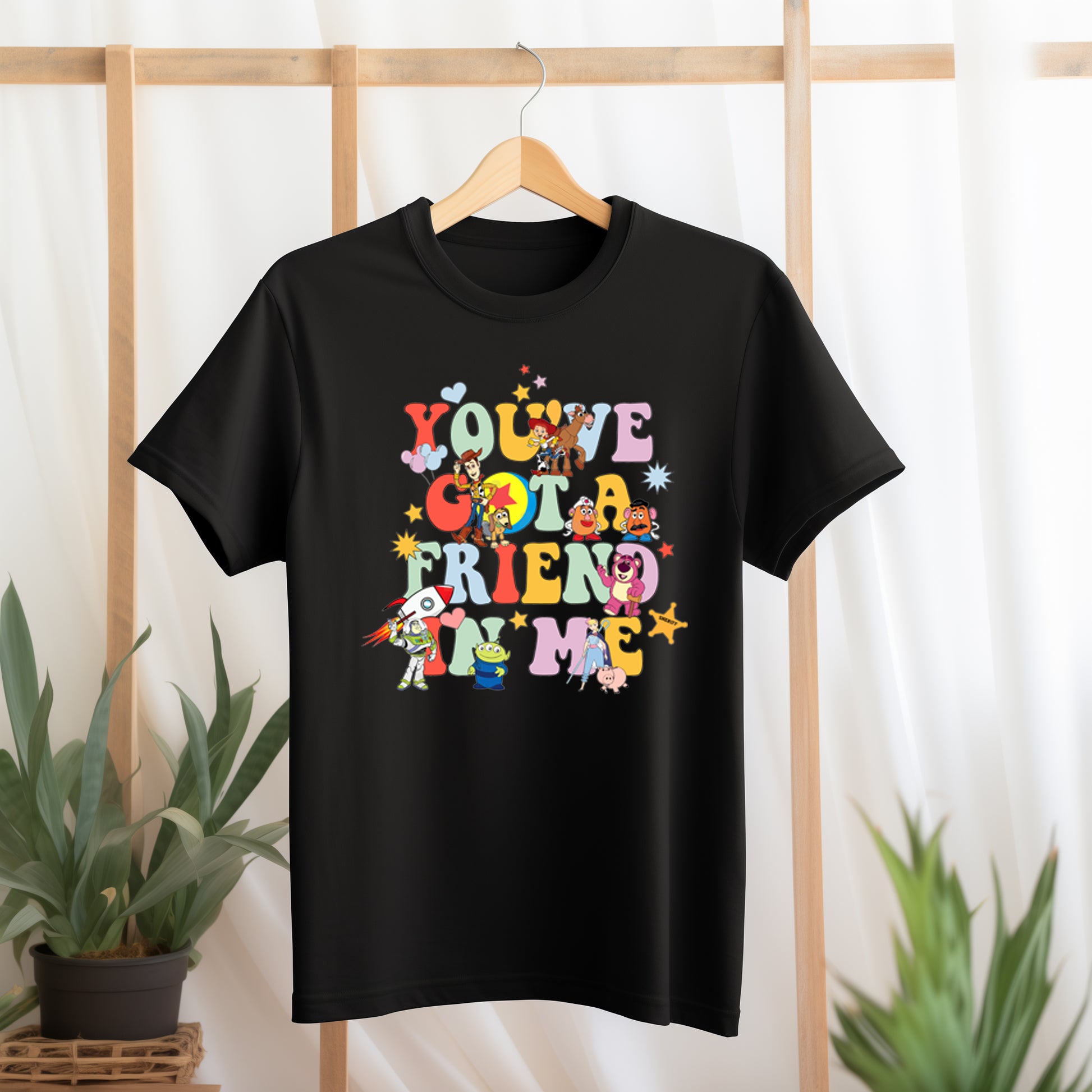 Black t-shirt with colorful text and character graphics on a hanger against a light background.