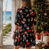 Woman in a festive dress standing on a beach with a decorated Christmas tree in the background.