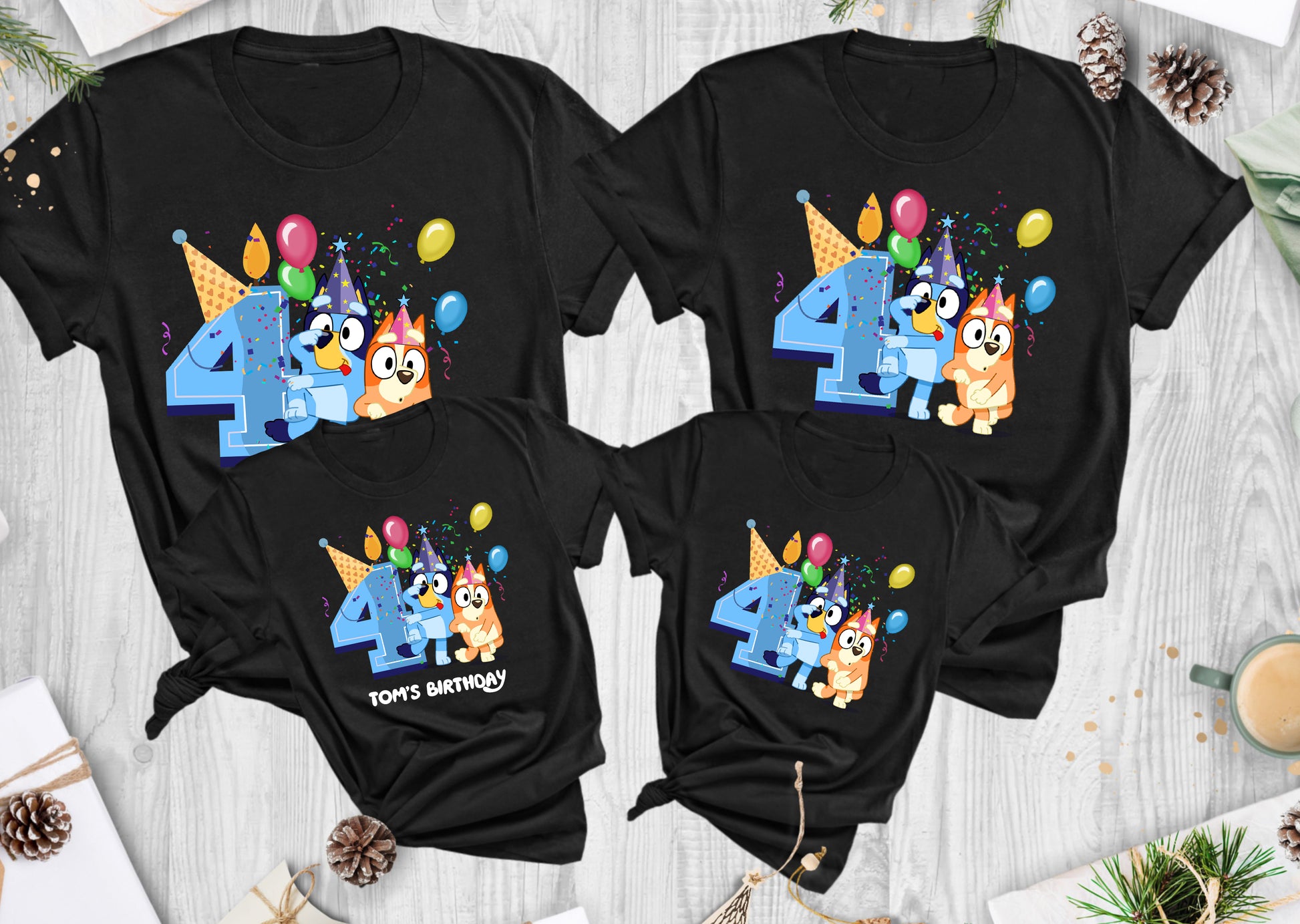 Four black t-shirts with colorful birthday designs on a wooden surface.