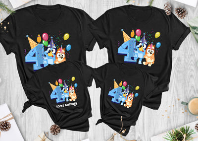 Four black t-shirts with colorful birthday designs on a wooden surface.