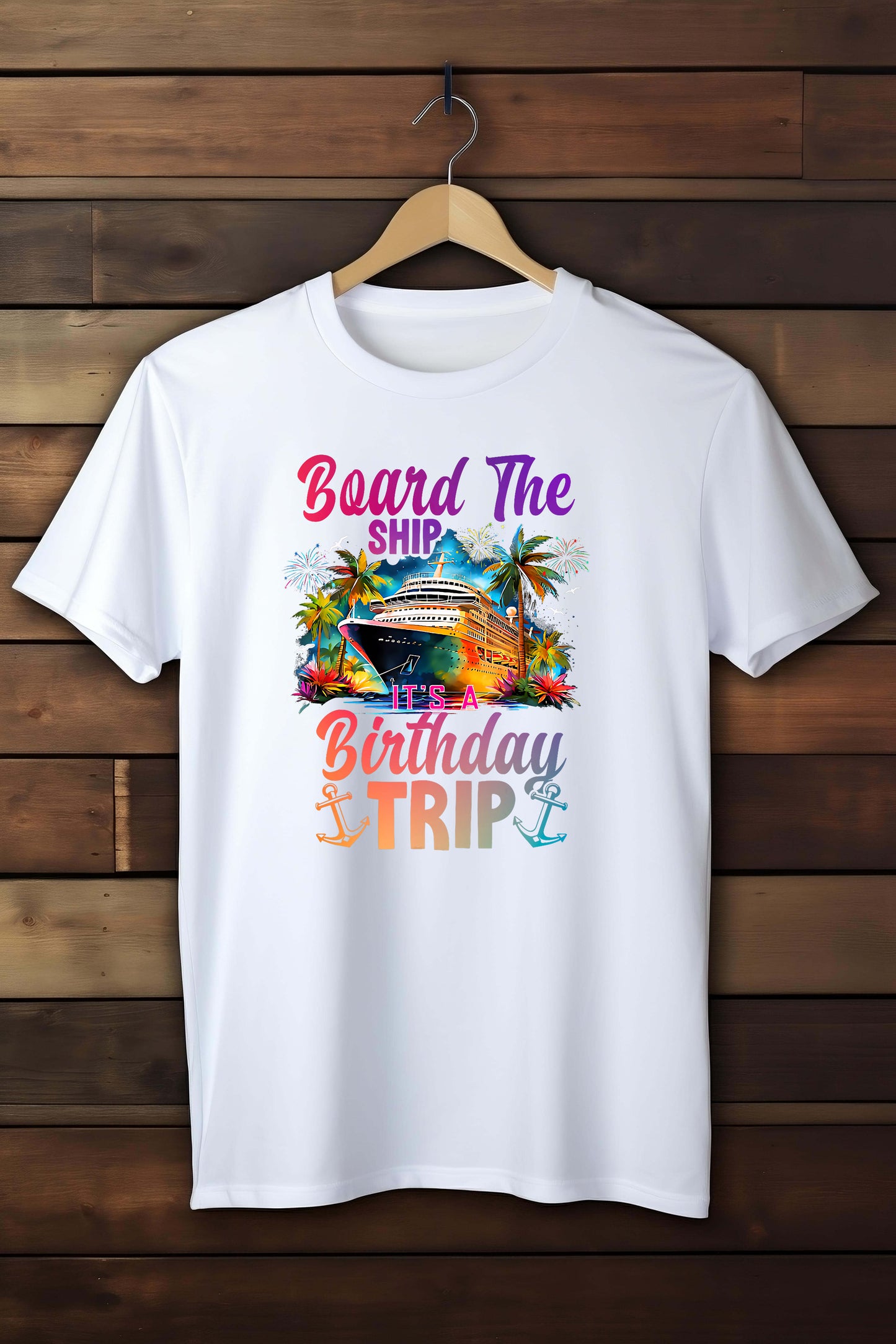 White t-shirt with a colorful graphic and text 'Board The Ship It's Birthday Trip' on a wooden background