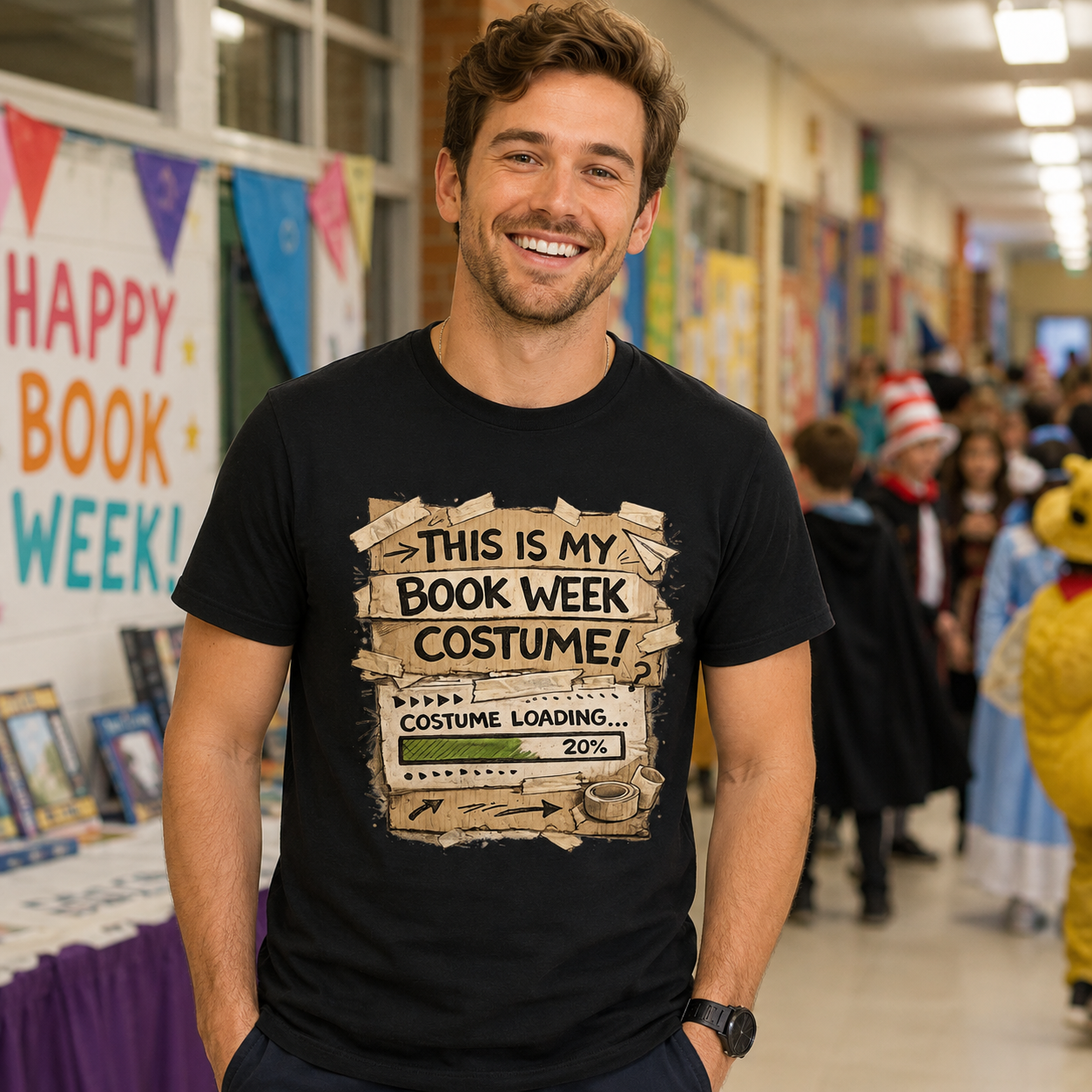 A smiling man in a school hallway wearing a black graphic t-shirt that reads 'THIS IS MY BOOK WEEK COSTUME WEEK! COSTUME LOADING.