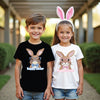Two children wearing 'Happy Easter' t-shirts with bunny designs outdoors.