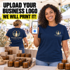 A smiling woman at an outdoor market wears a navy T-shirt with a printed 'Willow & Wick Candle Co.' logo on the chest and holds up a phone showing the same logo design.