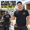 A smiling man in a black Brightwire Electrical t-shirt stands outdoors in front of a work van, holding up a smartphone that displays a custom business logo. Another man is visible in the background working at the van.