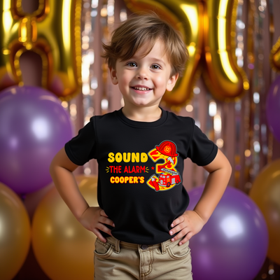 Child wearing a black t-shirt with a fire truck design and balloons in the background