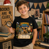 A smiling young boy stands in a cozy book-filled room wearing a black graphic T-shirt. The shirt features a colorful detective-themed print reading 'Book Week Quest Detective Agency' with an illustration of a mouse in a hat and a case file.