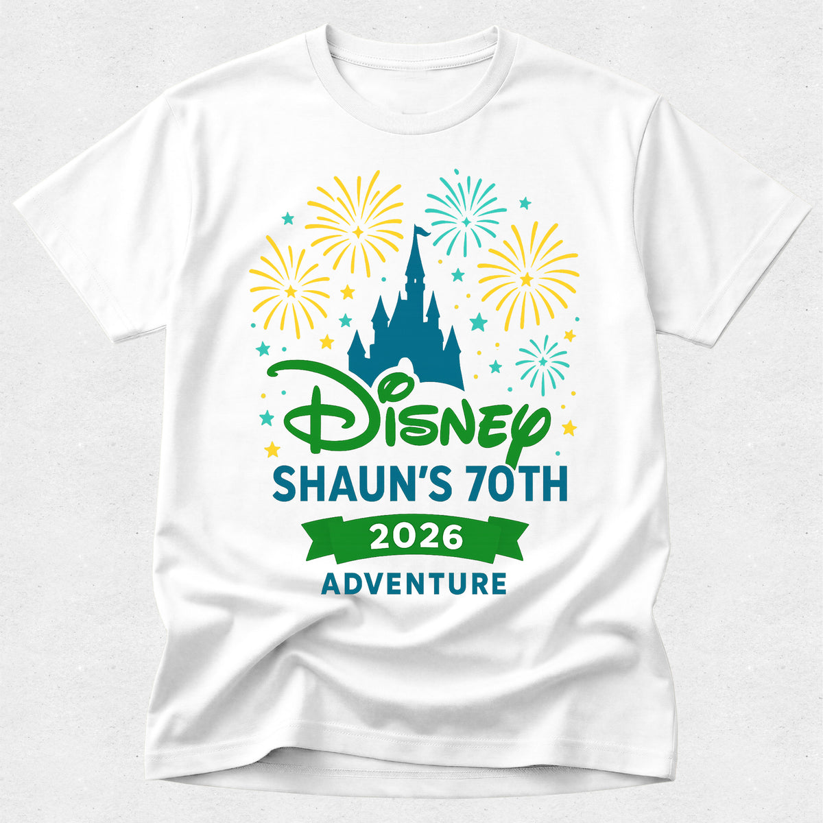 A white short-sleeve crewneck t-shirt featuring a colorful graphic print on the front. The design includes the Disney logo in green, the text 'SHAUN'S 70TH 2026 ADVENTURE' in blue and green, a teal castle silhouette, and yellow and teal fireworks in the background.