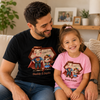 A man and a young girl sitting together on a beige couch, both wearing matching graphic T-shirts. The man wears a black T-shirt and the girl wears a pink T-shirt, both featuring a cartoon superhero design with the text 'Daddy & Layla'.