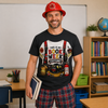 A man wearing a firefighter-themed graphic t-shirt and red plaid shorts stands in a classroom setting, holding a book. The t-shirt features a white graphic with red suspenders and the text 'THIS IS MY BOOK WEEK COSTUME!' alongside firefighter illustrations.