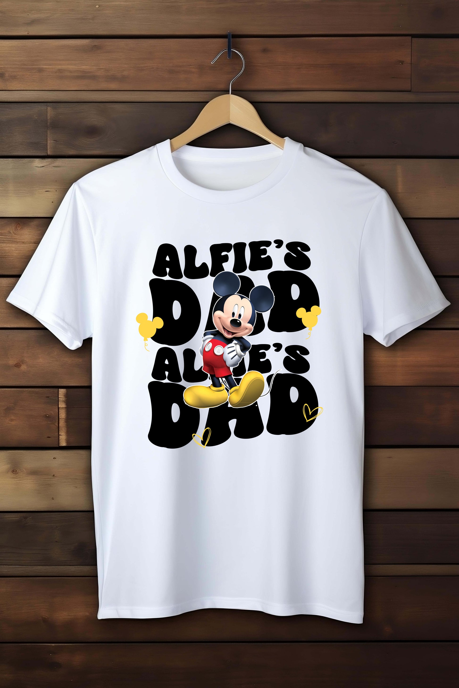 White t-shirt with a printed design of a character and text 'ALFIE'S DAD' on a wooden background
