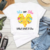 White t-shirt with 'He or She What Will It Bee' design on a wooden surface with jeans, sneakers, and a phone.