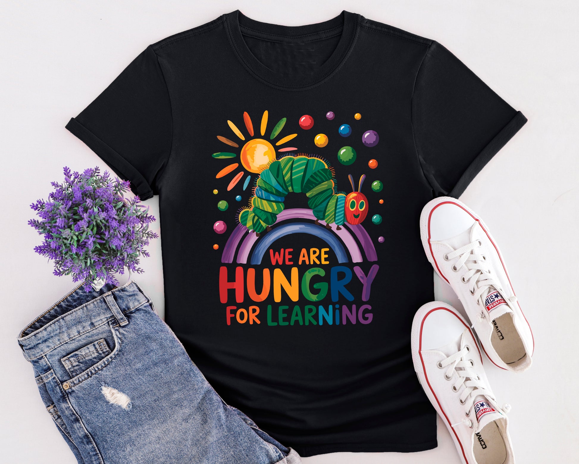 Flat lay of “Hungry for Learning” t-shirt featuring colourful caterpillar design inspired by classic children’s book.