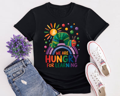 Flat lay of “Hungry for Learning” t-shirt featuring colourful caterpillar design inspired by classic children’s book.