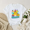 White t-shirt with Pikachu birthday design on a beige surface with flowers and a mug.