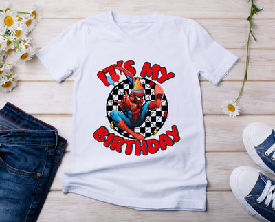White t-shirt with Spider-Man graphic and 'It's My Birthday' text on a wooden surface with jeans and shoes.