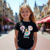 Child wearing a black Disney t-shirt with a character design in front of a theme park.