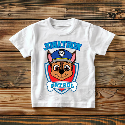 White t-shirt with a cartoon dog in a police uniform and 'Jonathon Patrol' text on a wooden surface