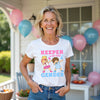 Woman wearing a white t-shirt with 'Keeper of the Gender' graphic in a celebratory outdoor setting with balloons.