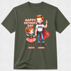 An olive green short-sleeve t-shirt with a colorful graphic of a cartoon dad and daughter dressed as superheroes, with the text 'HAPPY FATHER'S DAY' and 'GRACE DADDY'.