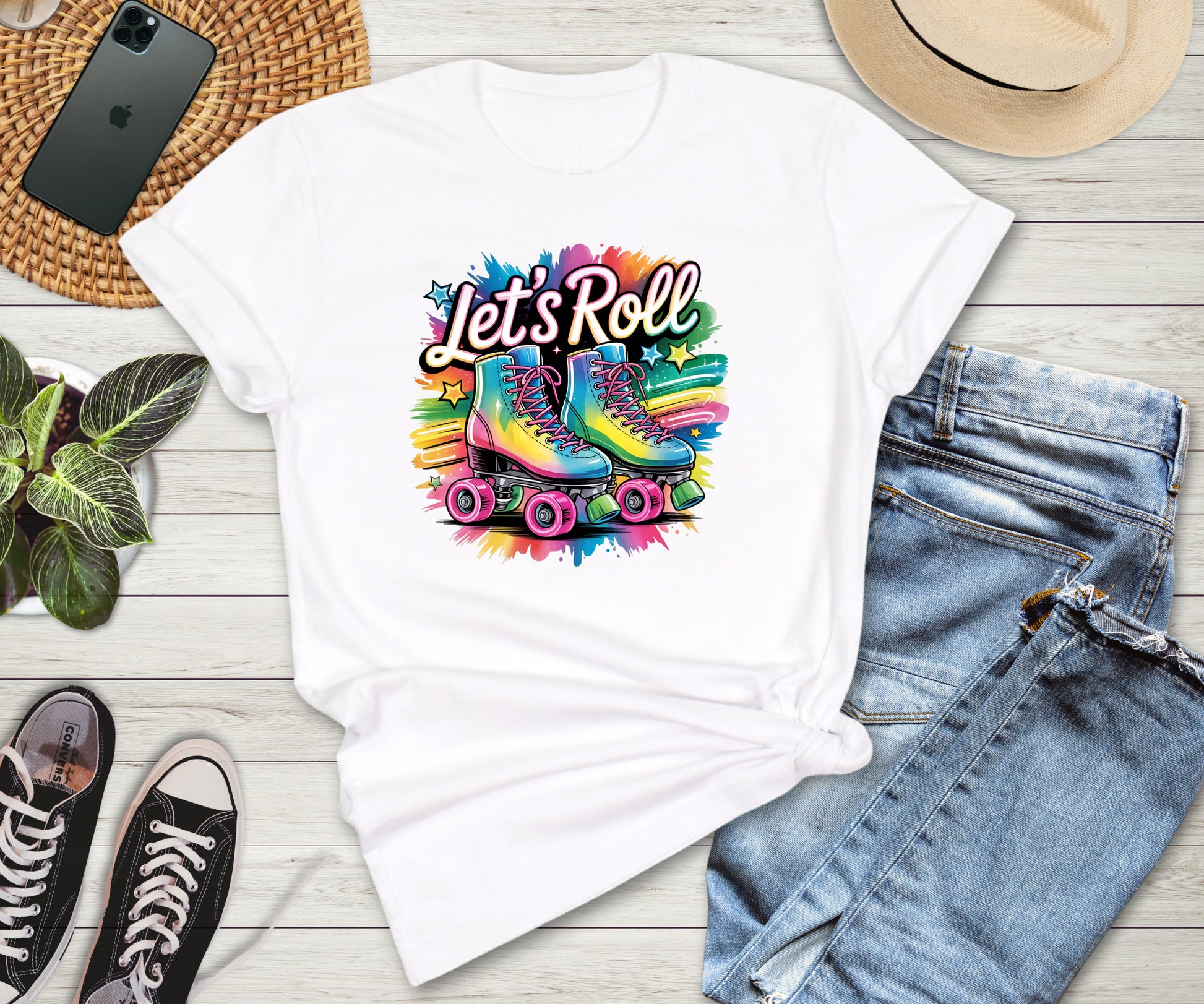 White t-shirt with colorful roller skates graphic and 'Let's Roll' text on a wooden surface with jeans and sneakers.