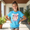 Young girl wearing a blue t-shirt with a colorful graphic design outdoors.