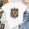 White t-shirt with Mardi Gras design on a wooden surface with jeans, sneakers, and a hat.