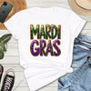 White t-shirt with 'Mardi Gras' text on a wooden surface with jeans, sneakers, and a hat.