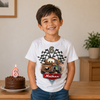 Child wearing a white t-shirt with a car graphic and number 6, standing next to a chocolate cake with a number 6 candle.