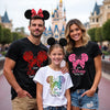 Family of three wearing Disney-themed shirts and Mickey Mouse ears in front of a castle.
