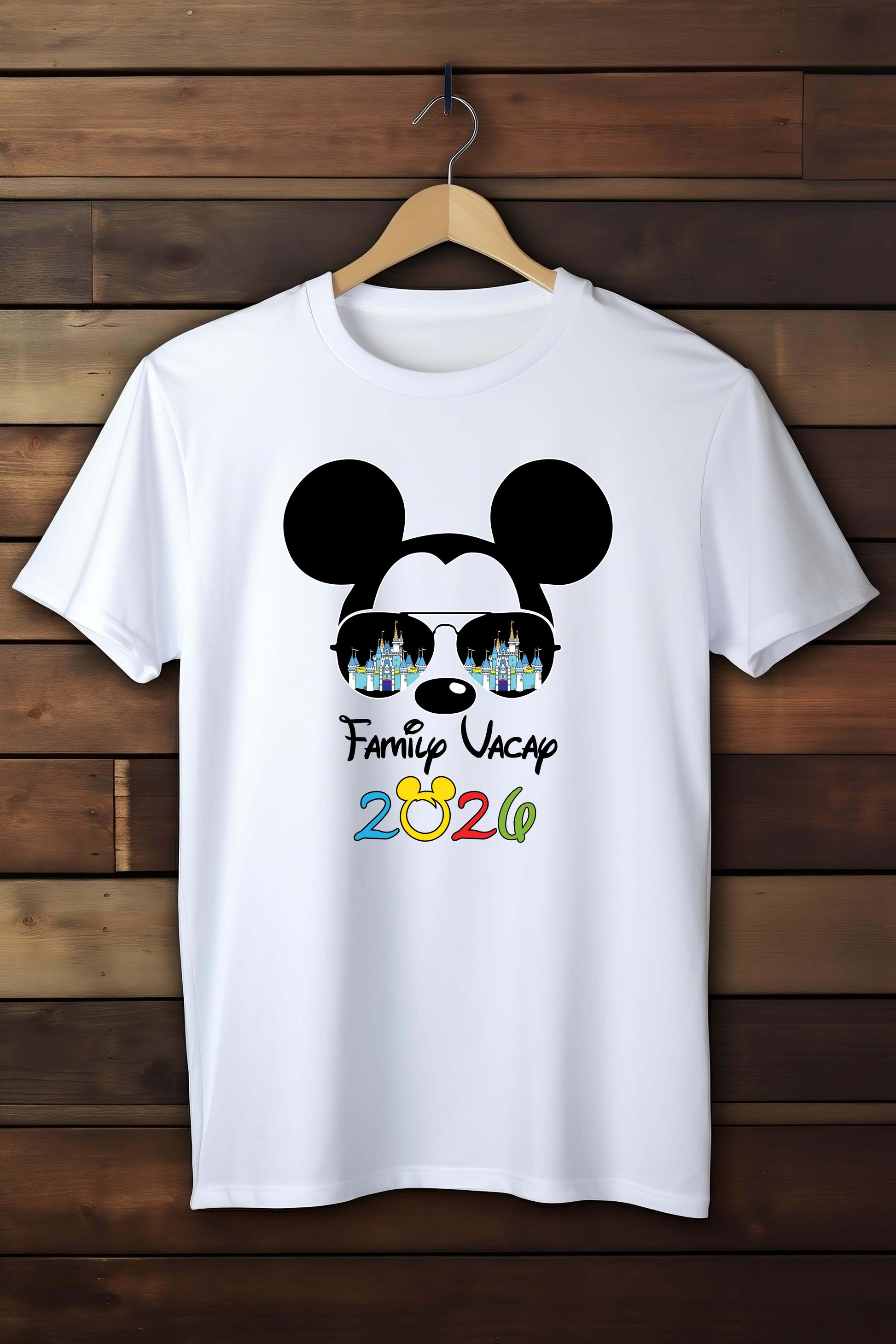 White t-shirt with a graphic design of a face with Mickey Mouse ears and 'Family Vacation 2026' text, hanging on a wooden wall.