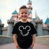 Child wearing a black t-shirt with a Disney 2026 design in front of a castle.